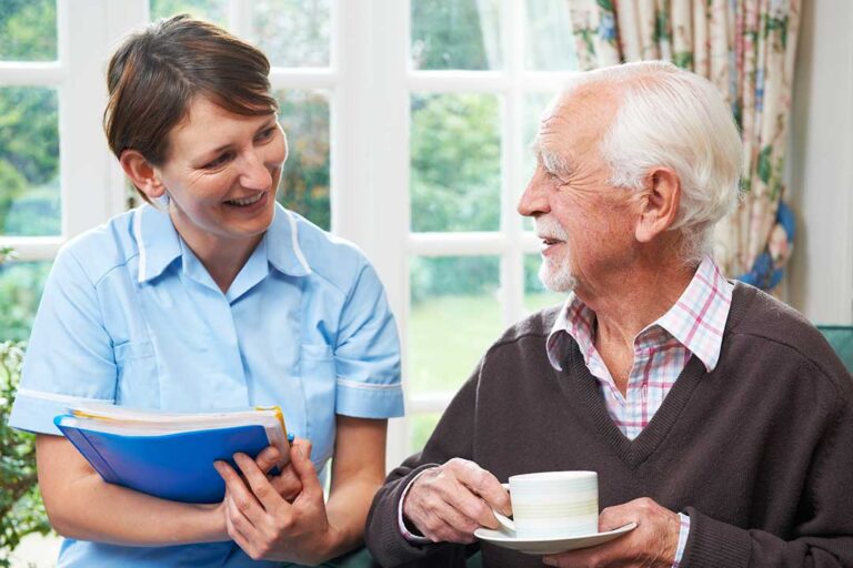 Two senior residents and a healthcare staff member review a medication chart together at a shared table indoors.